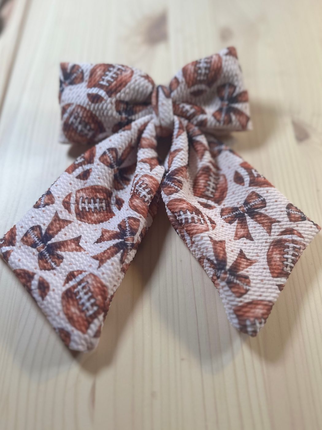 Handmade sailor bow in a cream print scattered with russet footballs and little tied bows