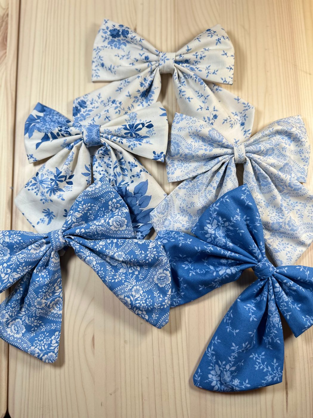 Five handmade sailor bows in blue and white floral cottons, laid out together on pale wood