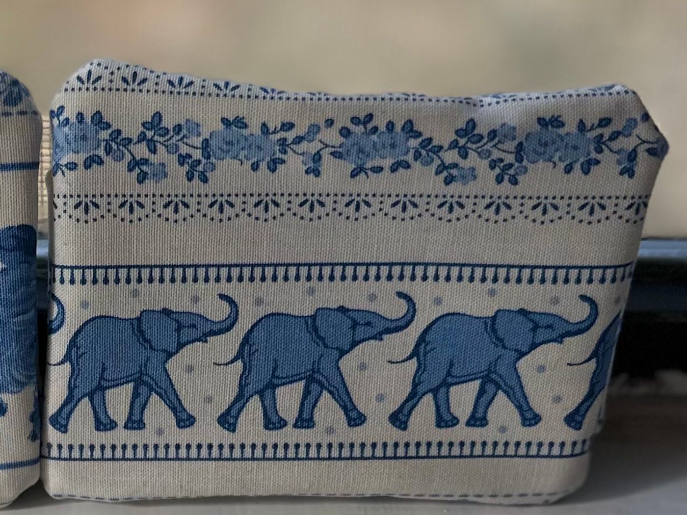 A small handmade fabric gift card holder, cream with a row of blue elephants walking trunk to tail across it