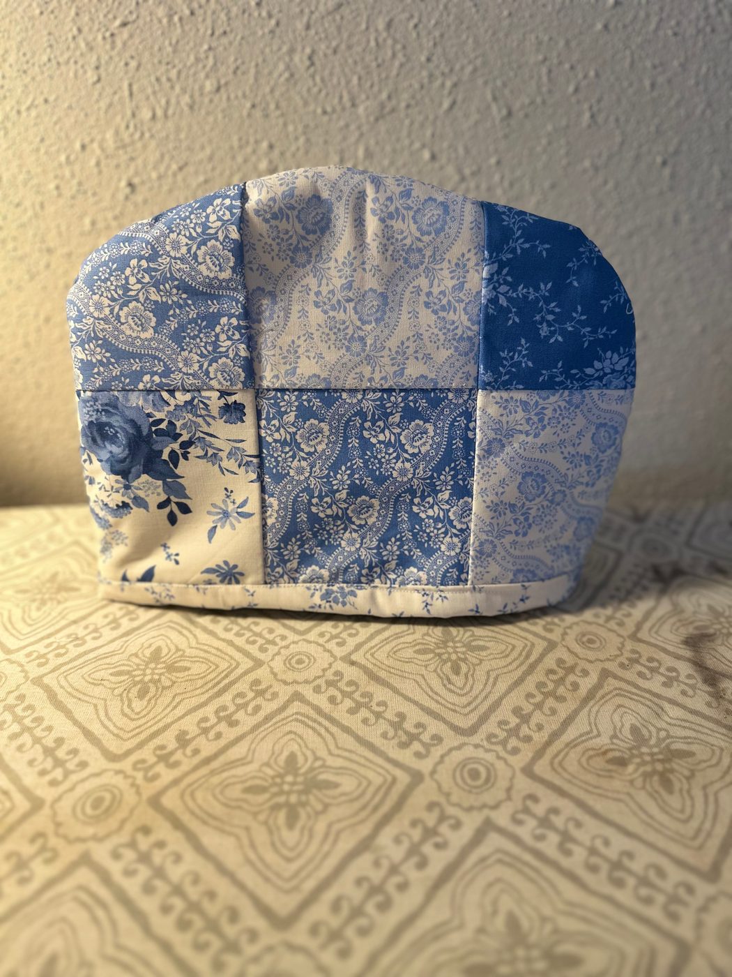Handmade patchwork tea cover in blue and white florals, paisleys and lace prints, with a bound cream hem