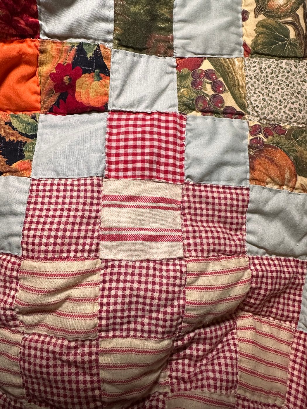 The same patch of quilt, mended — the gingham and ticking matched closely enough that the repair can't be picked out