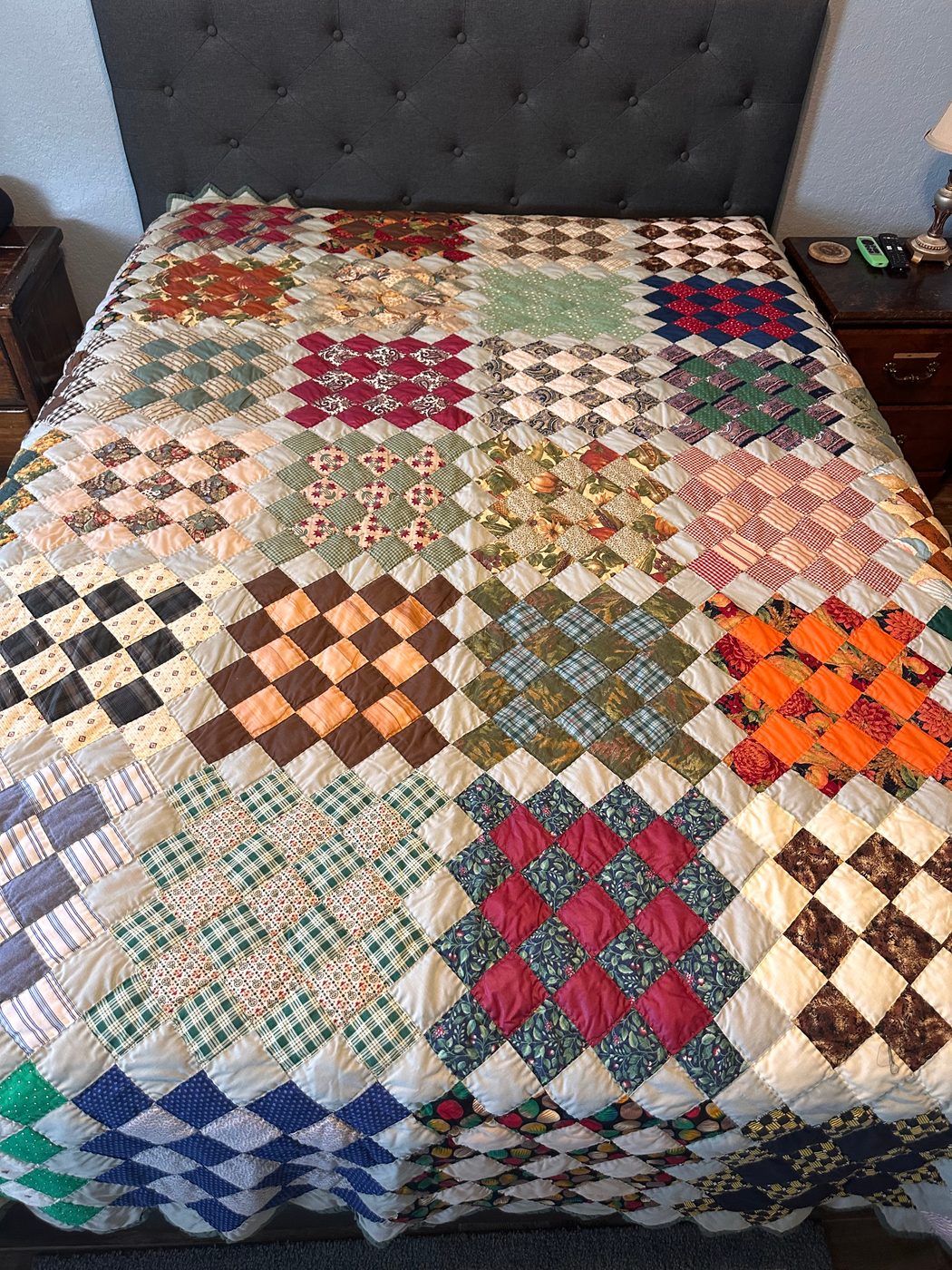 A thirty-year-old scrappy nine-patch quilt in many prints with cream sashing, spread across a bed. The mended section is not visible.