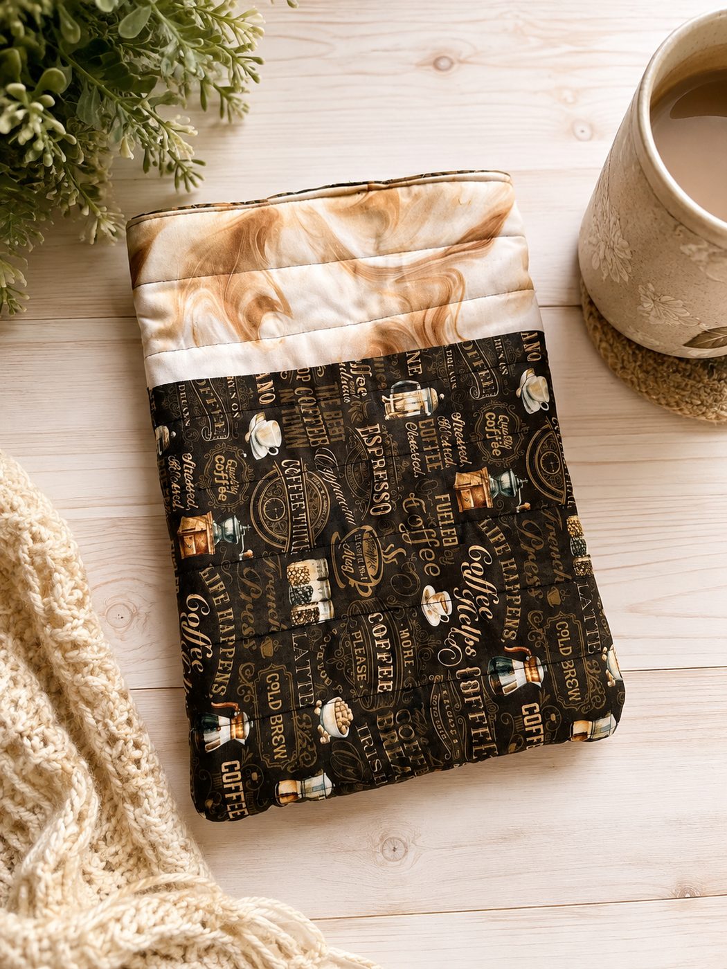 Handmade quilted book sleeve in a dark coffee-house print with a cream marble band, shown open to a toffee windowpane lining