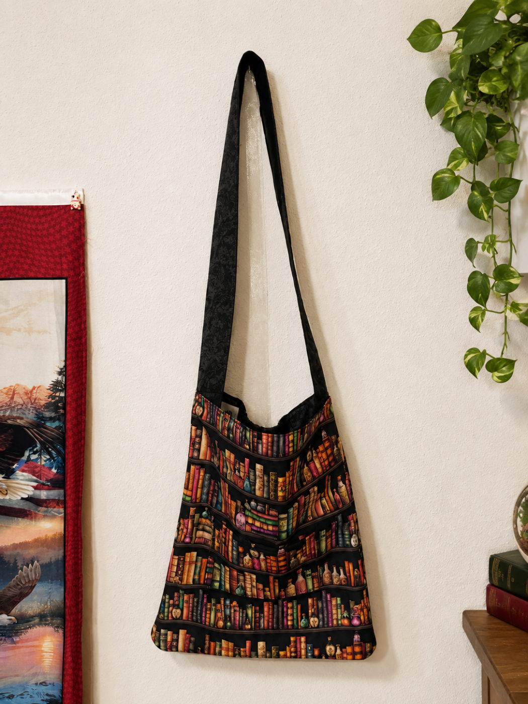 Handmade tote printed with shelves of antique books and potion bottles on black, hanging from a long black strap